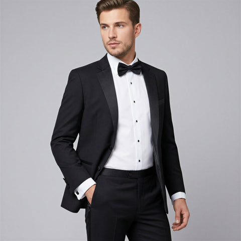 Man wearing a black tuxedo with a white shirt and bow tie on a gray background