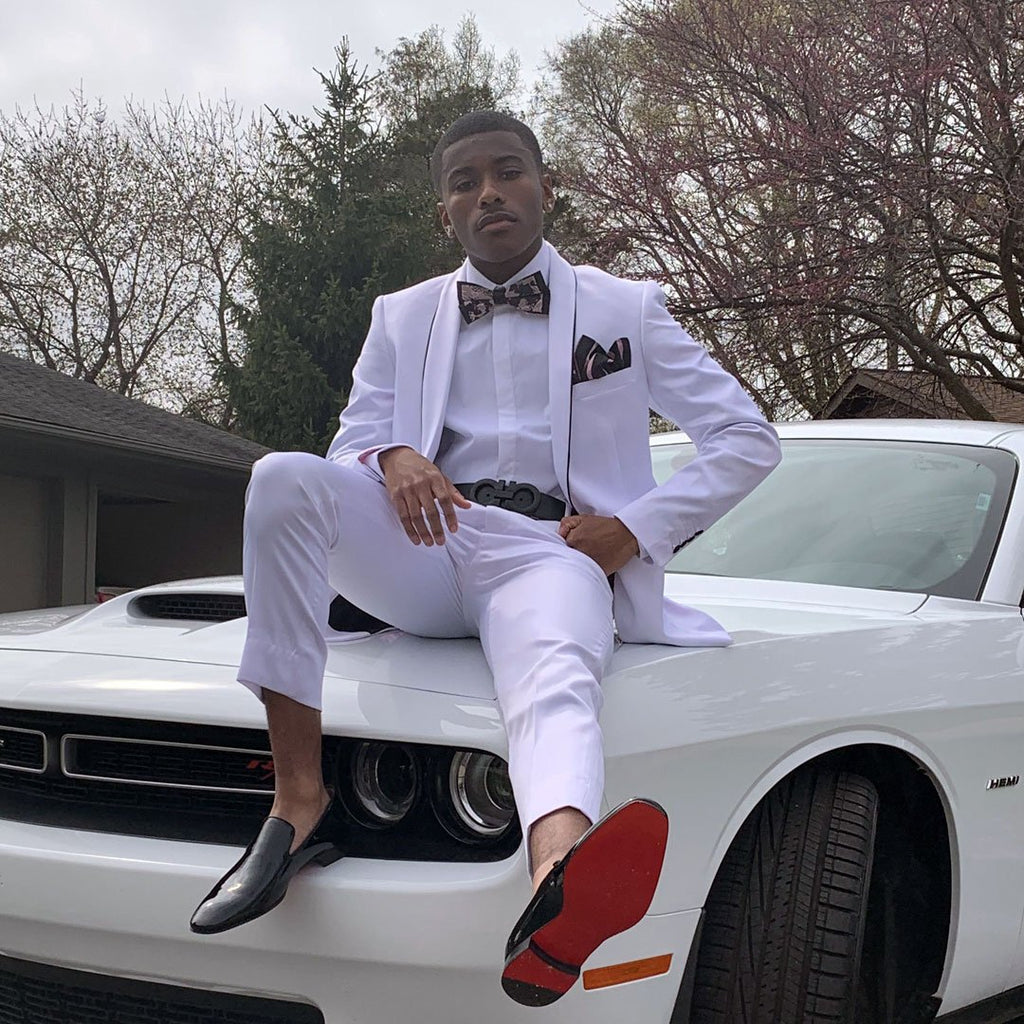guy wearing white prom suit sitting on top of car