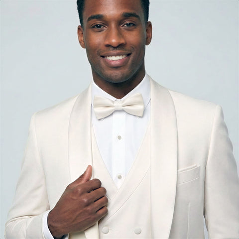 Man wearing a ivory shawl tuxedo with double breasted vest with a bow tie against a light gray background